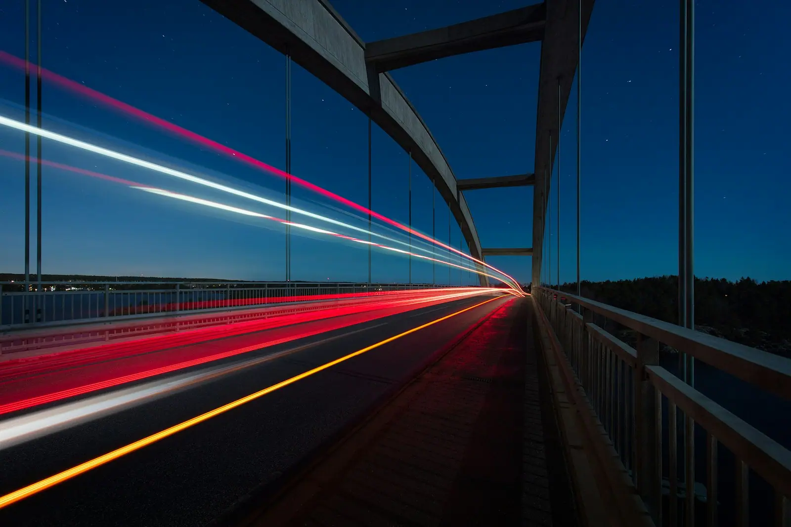 Suspension bridge at night with streaking vehicle light trails under a deep blue sky